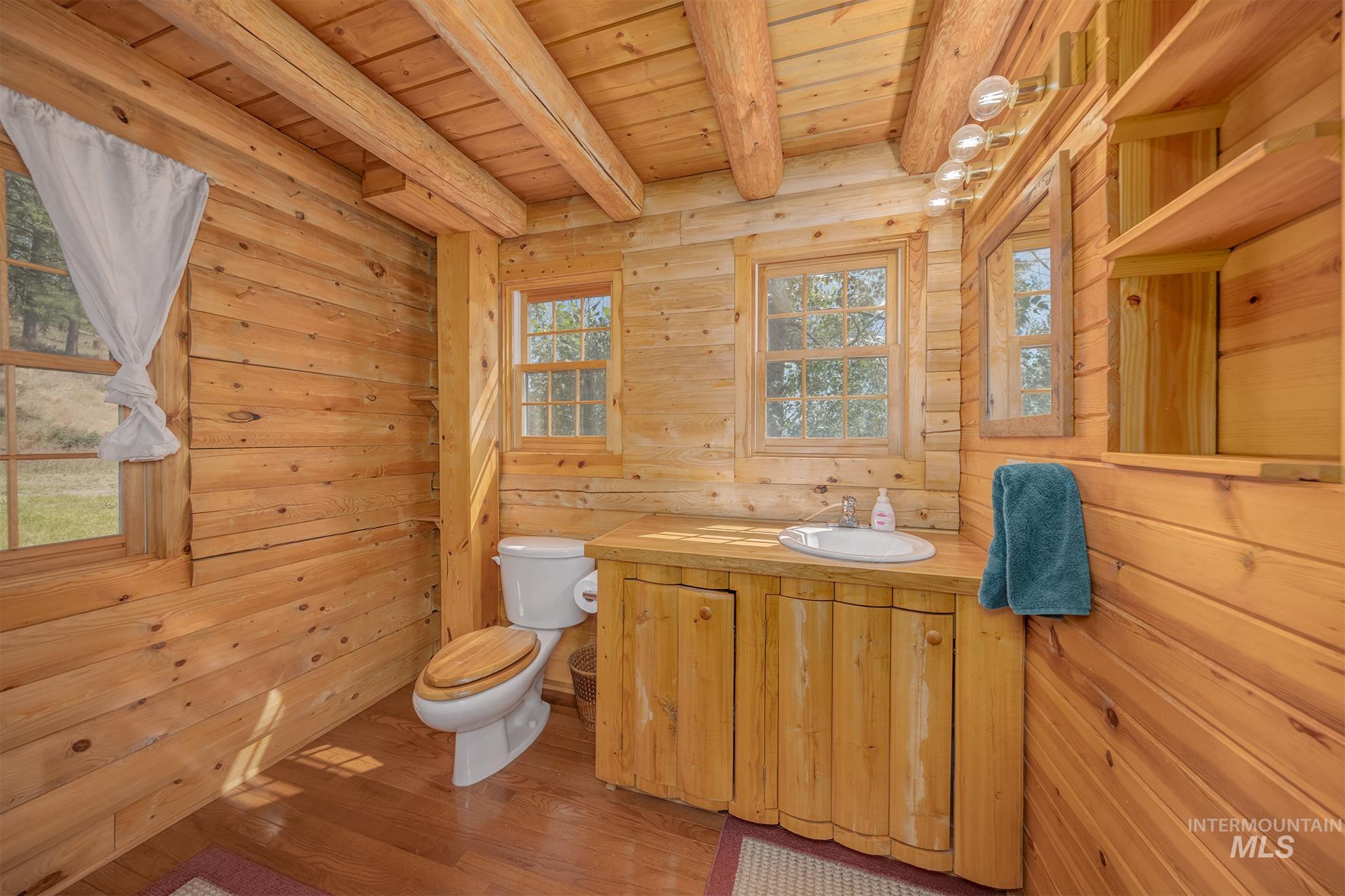 2150 Seid Creek Road Cambridge, ID 83610 - Photo 38 of 50 Wood-paneled bathroom featuring wood-finish flooring, exposed wood ceiling beams, a single vanity with storage, and two windows