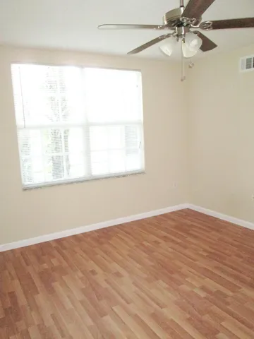 an empty room with wooden floor fan and windows