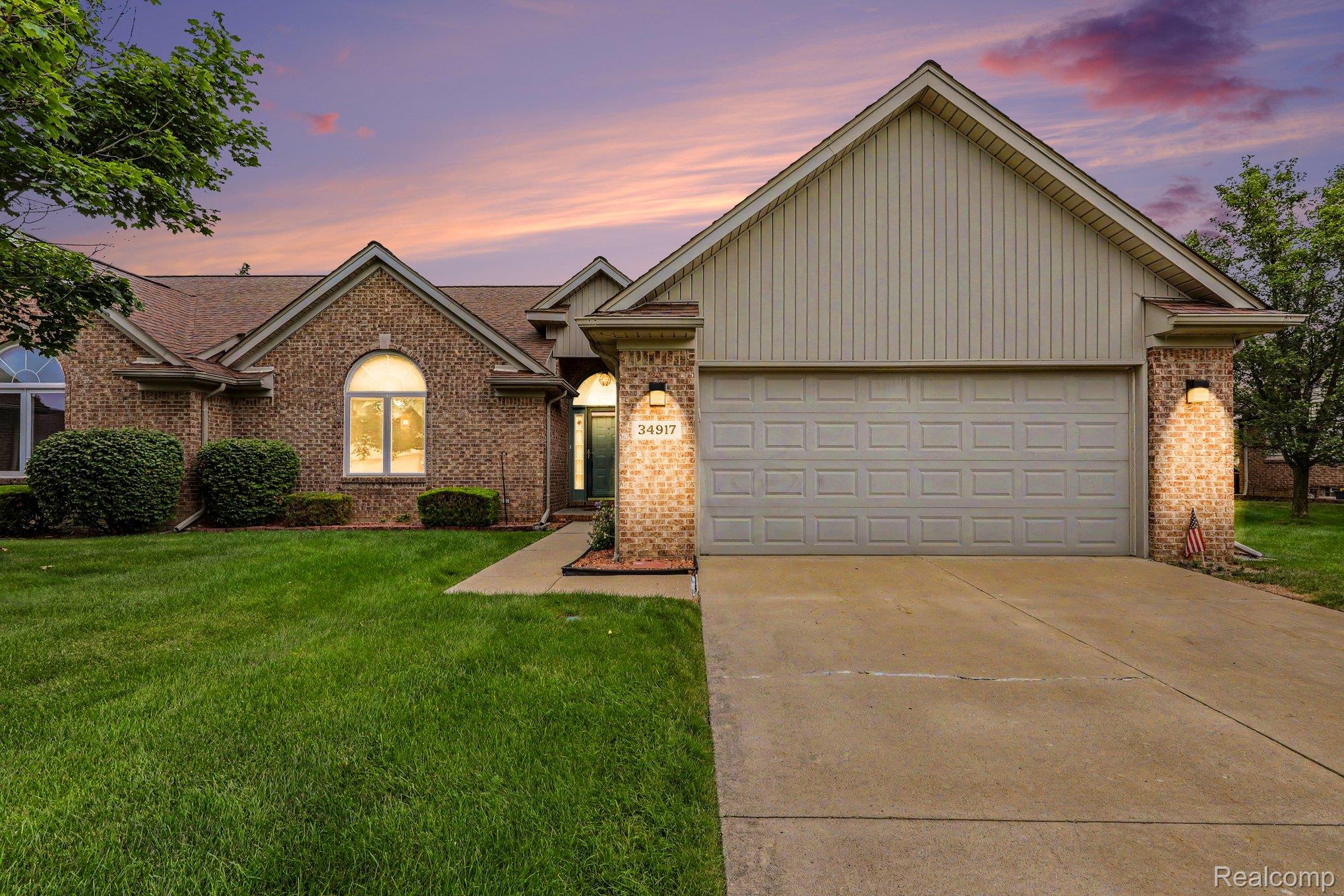 34917 Chickadee Ridge Richmond, MI 48062 - Photo 1 of 32 Brick exterior with a prominent arched window, attached garage, well-maintained lawn, and a concrete driveway