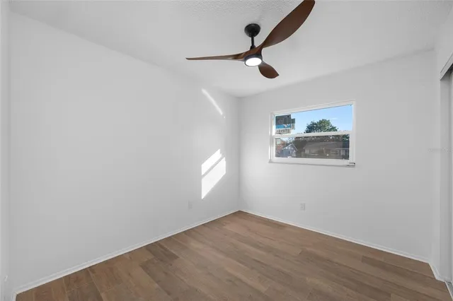 an empty room with wooden floor ceiling fan and windows