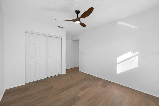 an empty room with wooden floor ceiling fan and windows