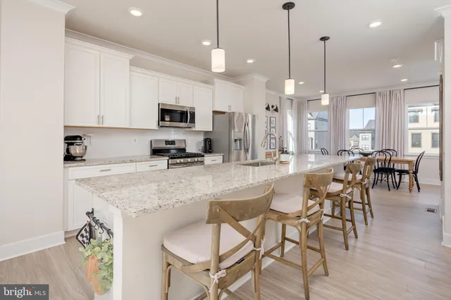 a kitchen with stainless steel appliances granite countertop a stove a sink a refrigerator a dining table and chairs with wooden floor