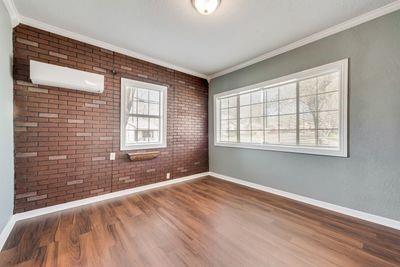 930 Freeman Street Sherman, TX 75092 - Photo 6 of 18 Spacious room featuring wood-finish flooring, a brick accent wall, and a large multi-pane window