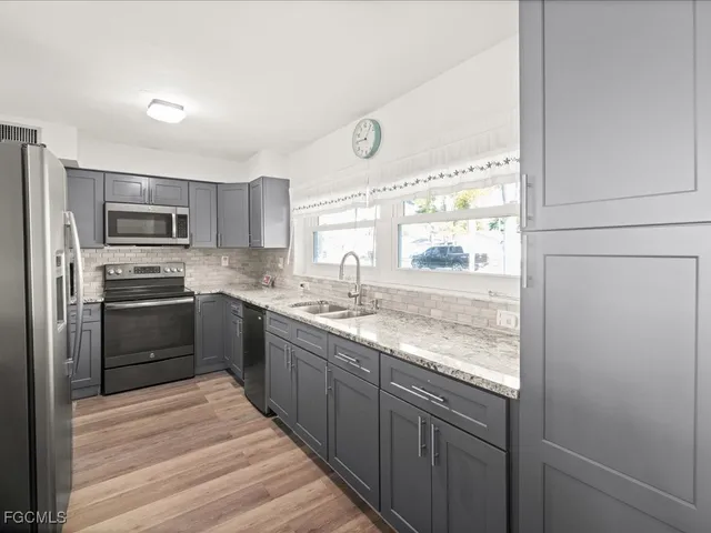 a kitchen with stainless steel appliances granite countertop a refrigerator a sink dishwasher a stove and a microwave oven with wooden floor