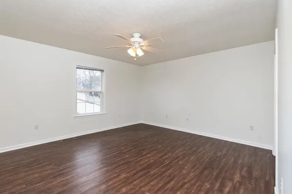 an empty room with wooden floor fan and windows
