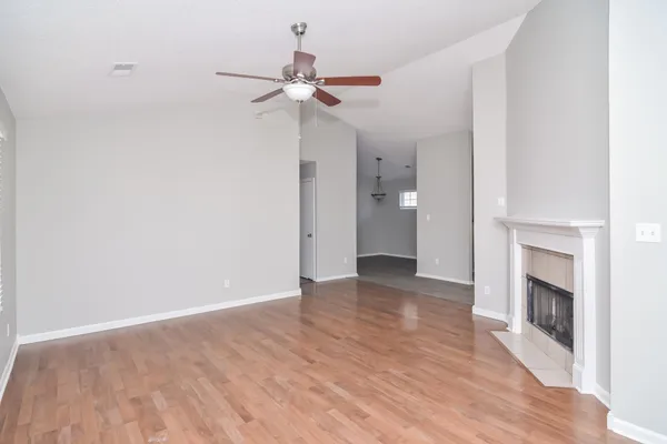 an empty room with wooden floor fan and windows