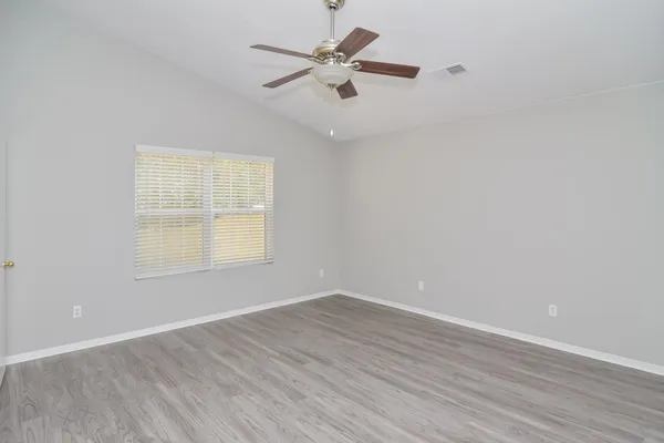 an empty room with wooden floor ceiling fan and windows