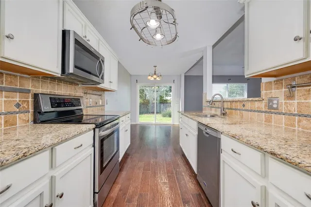 a large kitchen with granite countertop a stove top oven a sink dishwasher a dining table and chairs with wooden floor