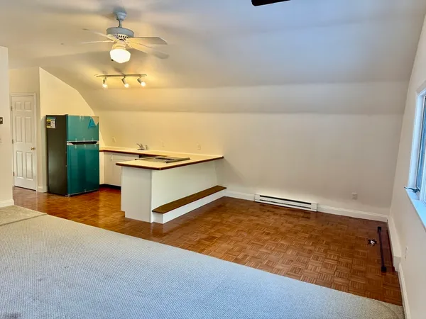 an empty room with a chandelier fan and kitchen view
