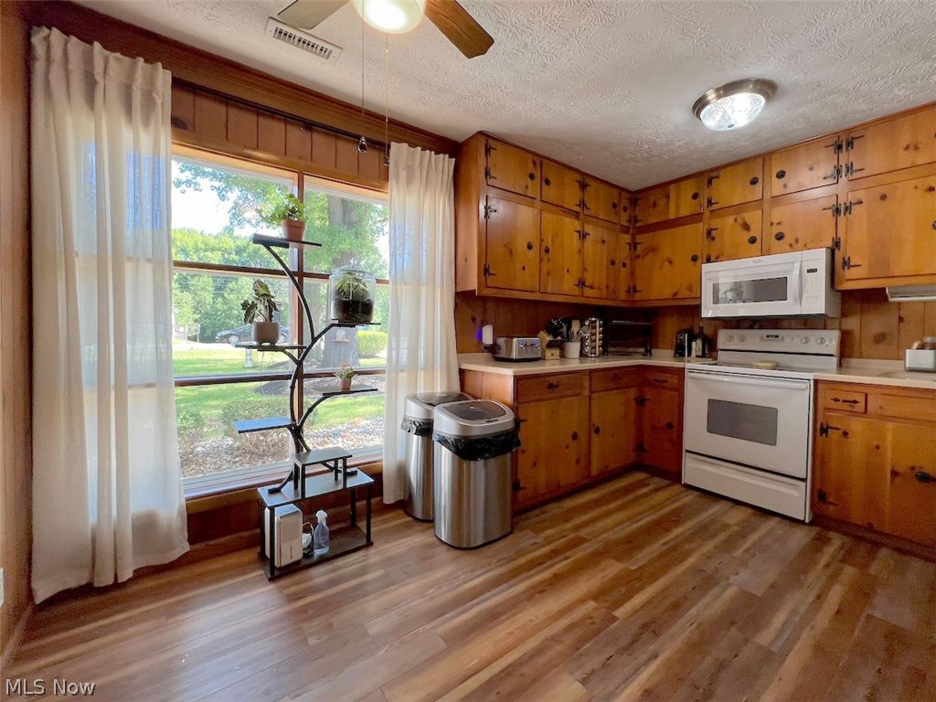 Wood-finish flooring, wood cabinetry with black hardware, white built-in microwave, white electric range, and a large window