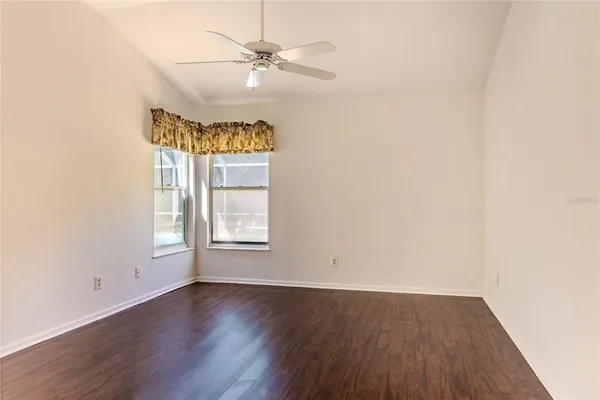 an empty room with wooden floor chandelier fan and windows