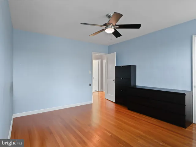 a view of an empty room with wooden floor and a ceiling fan