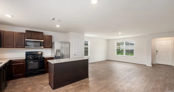 a kitchen with stainless steel appliances granite countertop a stove top oven a sink dishwasher and a refrigerator with wooden floor