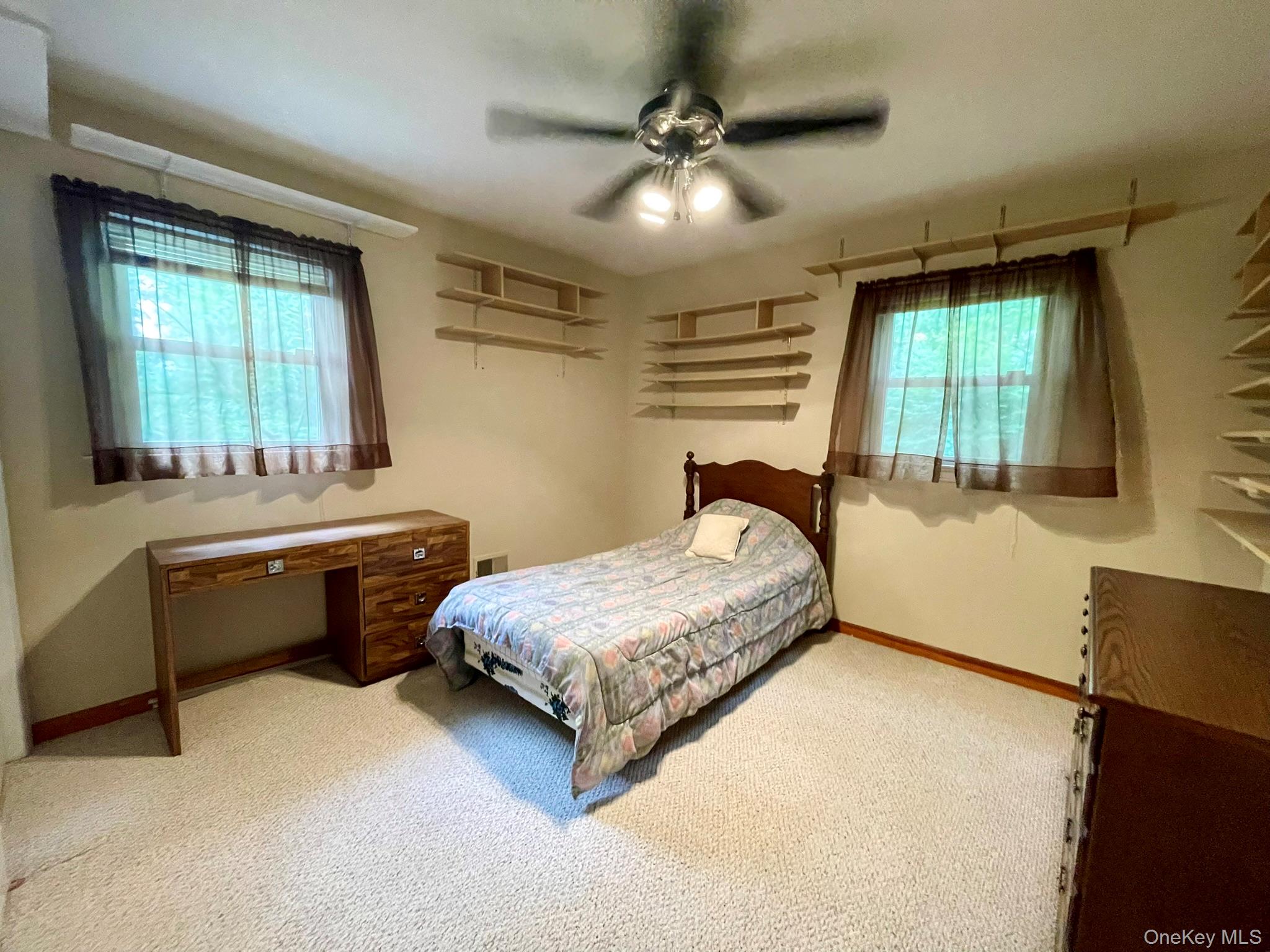21 Harmony Road Spring Valley, NY 10977 - Photo 15 of 24 Carpeted room featuring a ceiling fan with integrated lighting, two windows with brown sheer curtains, and multiple wall-mounted shelving units