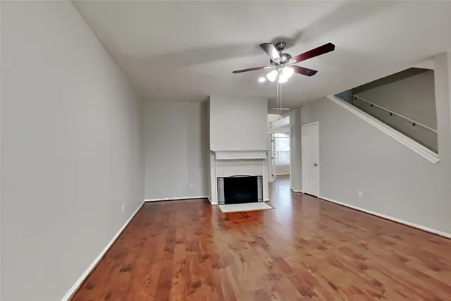 a view of an empty room with wooden floor a fireplace and a window