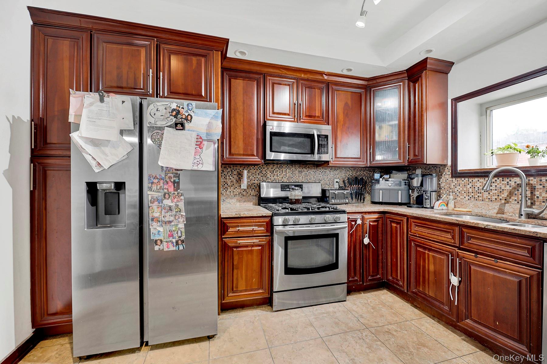 179-50 Anderson Road Queens, NY 11434 - Photo 18 of 23 Kitchen featuring stainless steel appliances, tasteful backsplash, light stone countertops, glass insert cabinets, and light tile patterned floors