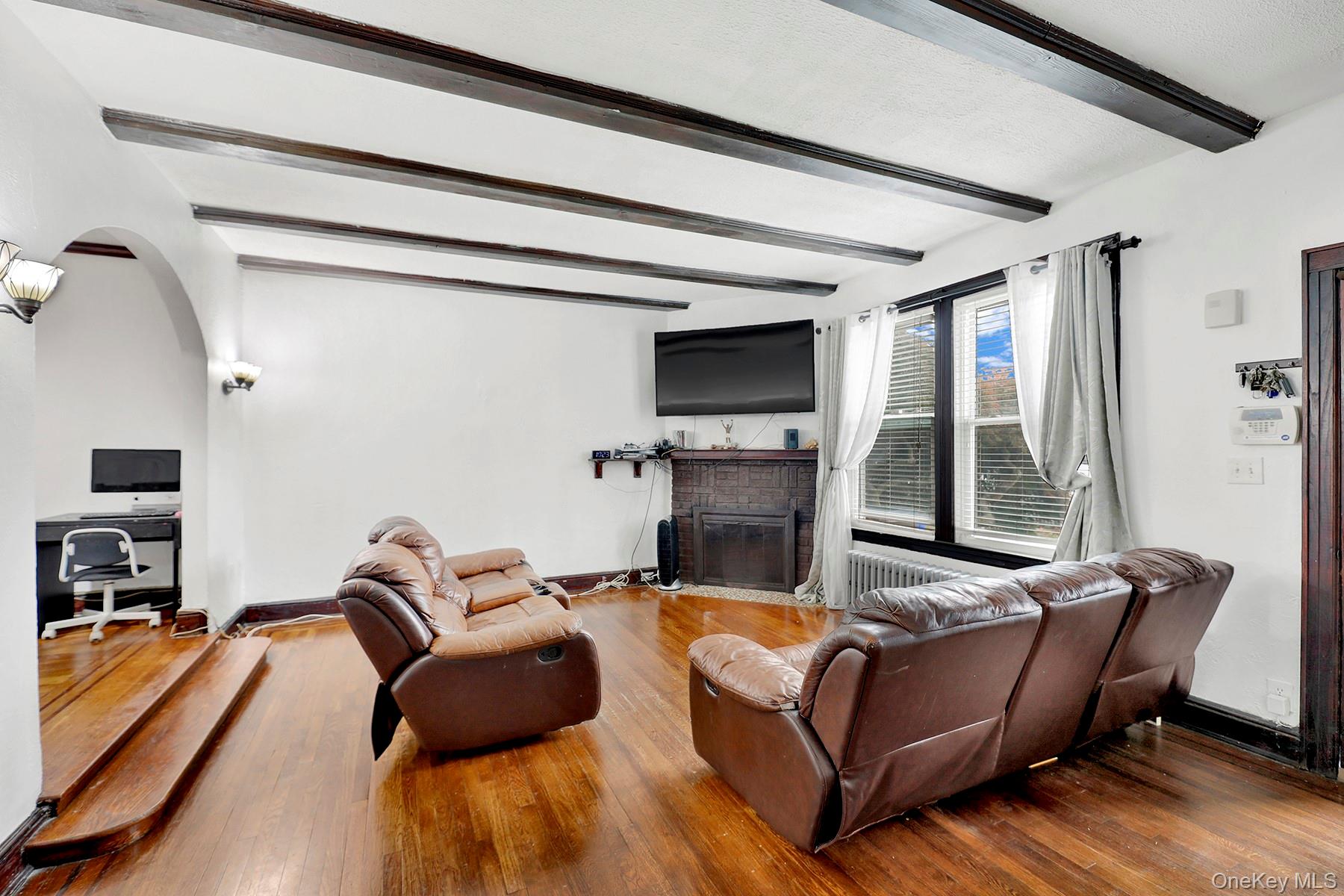179-50 Anderson Road Queens, NY 11434 - Photo 5 of 23 Living room with beamed ceiling, arched walkways, a brick fireplace, and wood finished floors