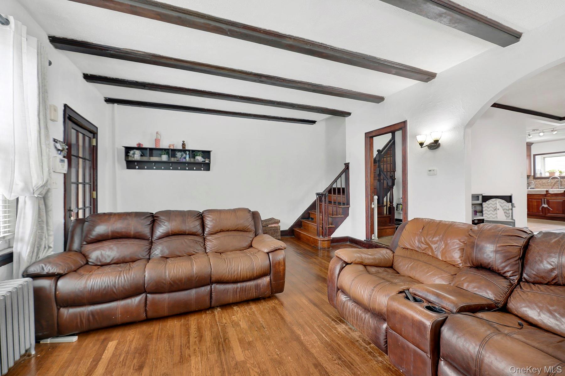 179-50 Anderson Road Queens, NY 11434 - Photo 6 of 23 Living area featuring radiator heating unit, arched walkways, wood finished floors, stairway, and beam ceiling