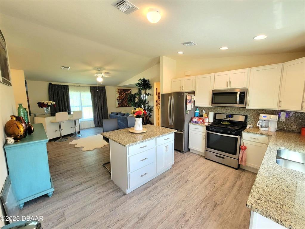 5023 Littlefield Road LaBelle, FL 33935 - Photo 7 of 36 a kitchen with stainless steel appliances kitchen island granite countertop a stove top oven a sink dishwasher a refrigerator and cabinets with wooden floor