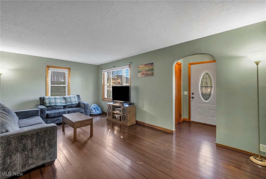 Living room featuring a textured ceiling, arched walkways, and dark wood-type flooring