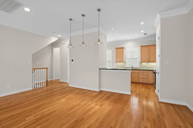 a view of an empty room with wooden floor and a kitchen view
