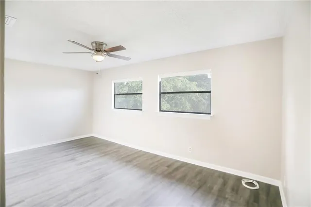 an empty room with wooden floor ceiling fan and window