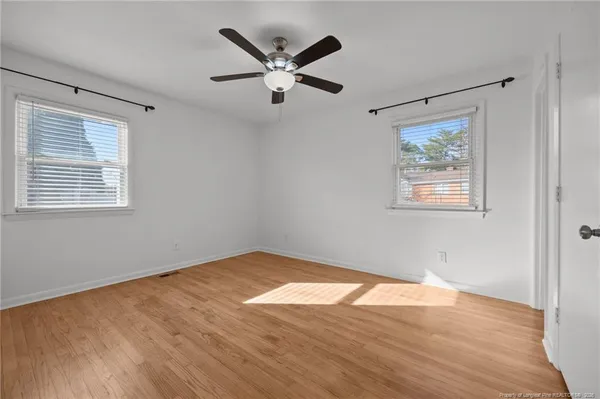 a view of an empty room with wooden floor and a ceiling fan