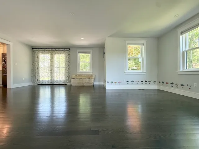 an empty room with wooden floor and windows with curtains