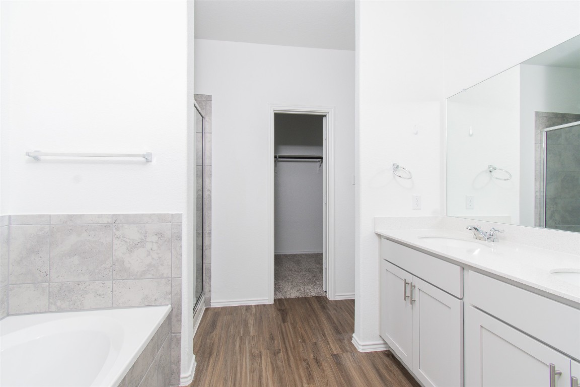 9101 Daisy Cutter Crossing Georgetown, TX 78626 - Photo 11 of 28 Bathroom with a stall shower, double vanity, a bath, wood finished floors, and a spacious closet