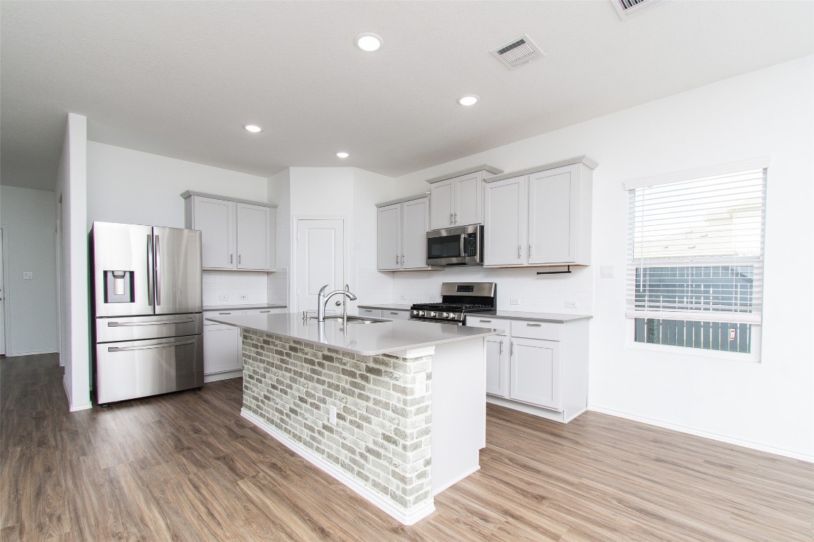 9101 Daisy Cutter Crossing Georgetown, TX 78626 - Photo 4 of 28 Kitchen featuring stainless steel appliances, light wood-style floors, a kitchen island with sink, decorative backsplash, and recessed lighting