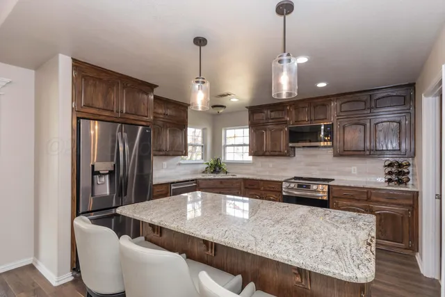 a kitchen with stainless steel appliances granite countertop a sink a stove a refrigerator and island