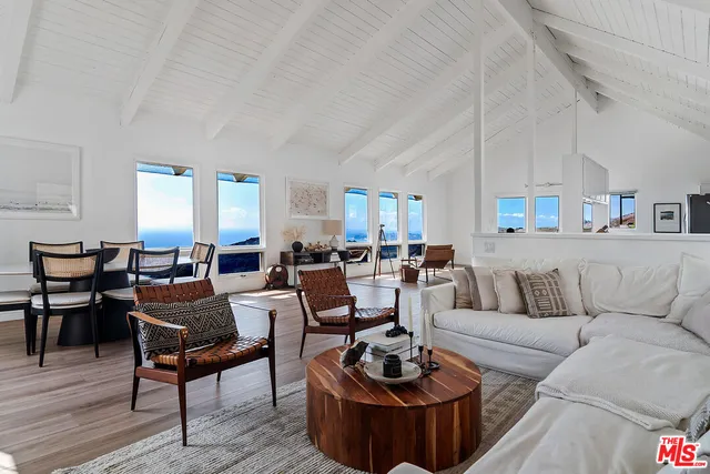 a living room with furniture a rug kitchen view and a large window