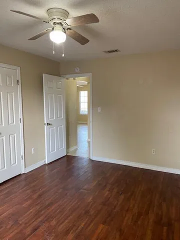 a view of an empty room with wooden floor and a ceiling fan