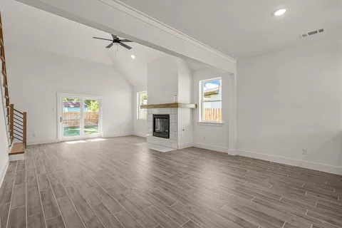 an empty room with wooden floor fireplace and windows