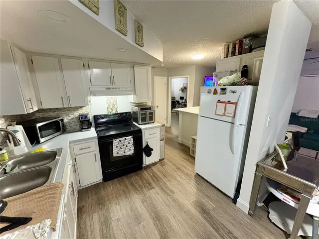 a kitchen with granite countertop a refrigerator a stove a sink dishwasher and white cabinets with wooden floor