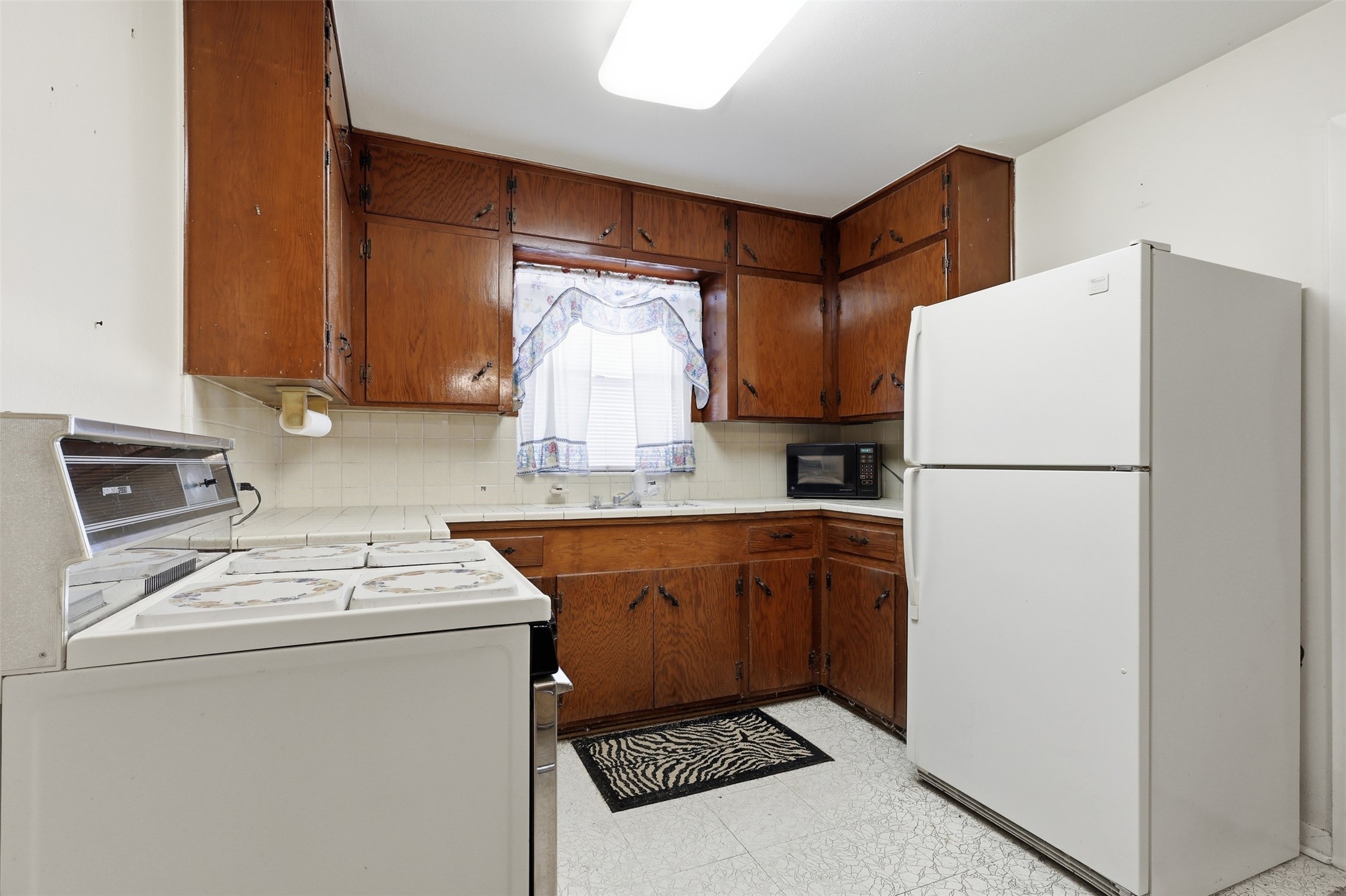 5707 Waltrip Street Houston, TX 77087 - Photo 5 of 15 Cozy kitchen with vintage charm, featuring wood cabinetry, a large refrigerator, and a classic stove. Bright window above the sink offers natural light.
