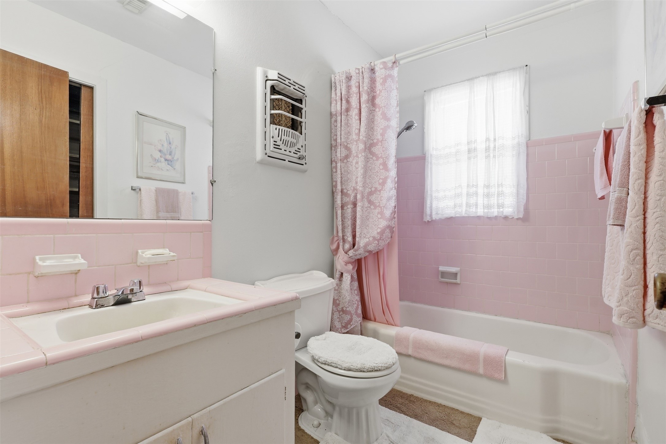 5707 Waltrip Street Houston, TX 77087 - Photo 10 of 15 This is a charming vintage-style bathroom featuring pink tiles. It has a light vanity with a pink countertop, a bathtub with a shower, and a window allowing natural light.