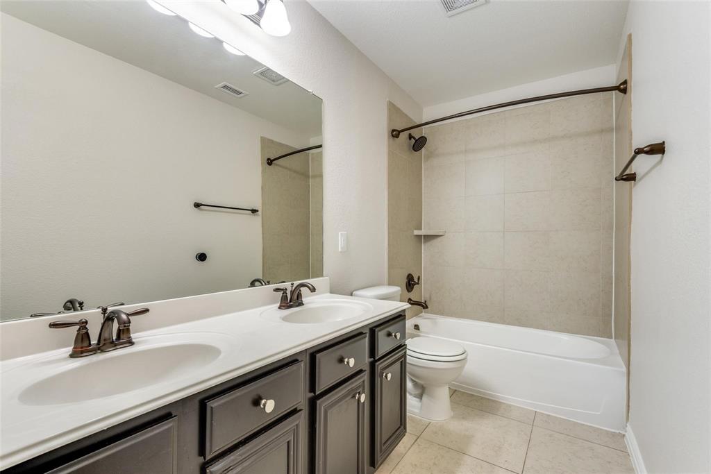 2344 Ranchview Drive Little Elm, TX 75068 - Photo 22 of 24 Bathroom featuring a double vanity with dark cabinetry and white countertops, bronze-finish fixtures, and a shower-tub combination with light-toned wall tile