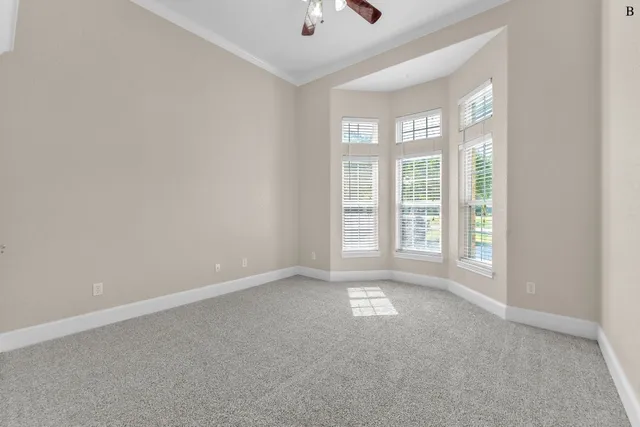an empty room with chandelier fan and windows