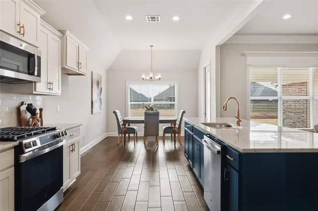 a kitchen with stainless steel appliances granite countertop a stove top oven a sink dishwasher a dining table and chairs with wooden floor