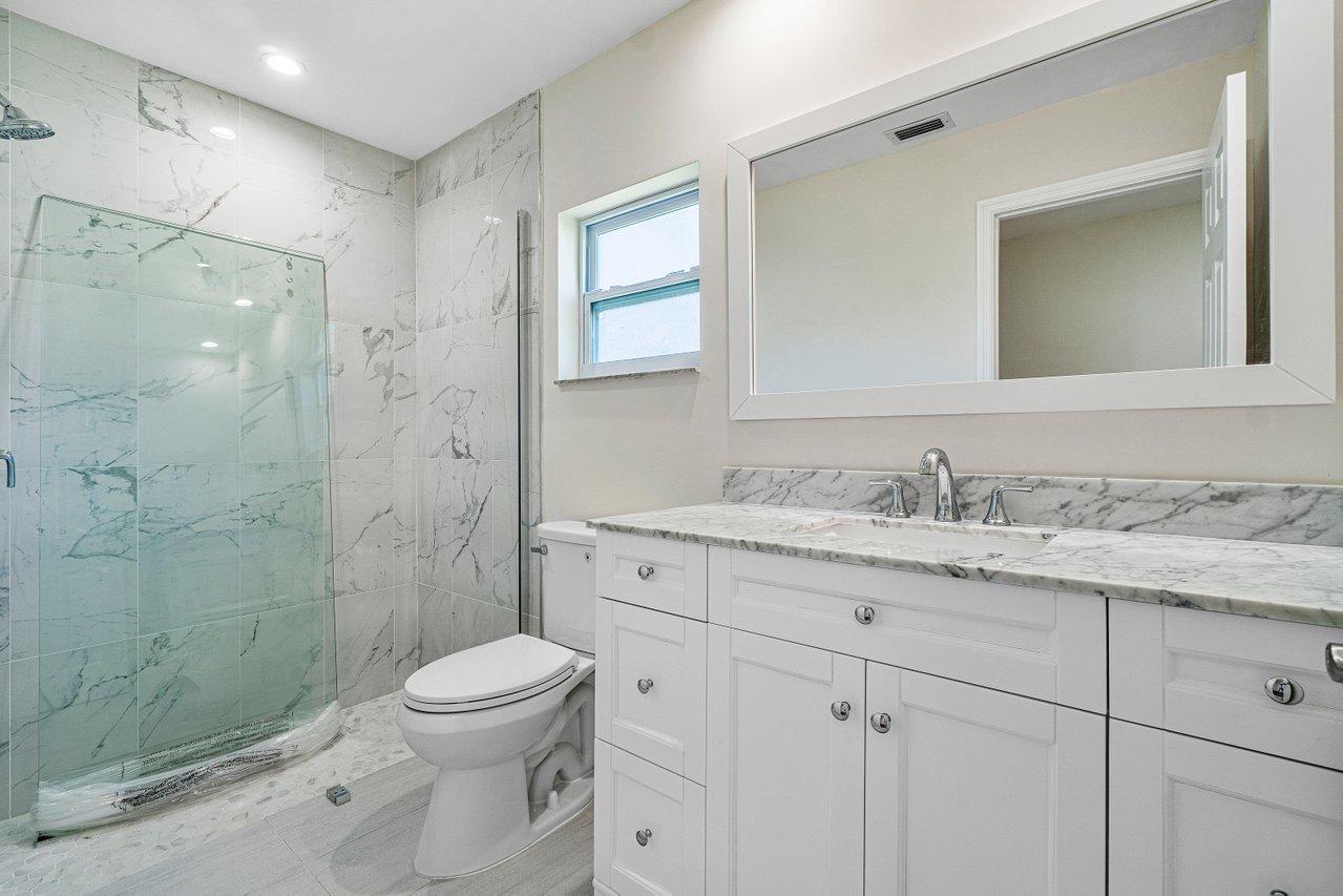 6359 Winding Brook Way Delray Beach, FL 33484 - Photo 13 of 24 a bathroom with a granite countertop toilet a sink a mirror and shower