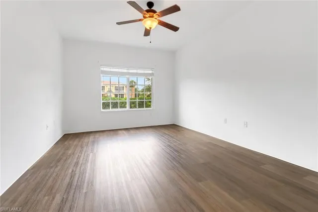 an empty room with wooden floor fan and windows