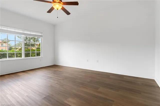an empty room with wooden floor chandelier fan and windows