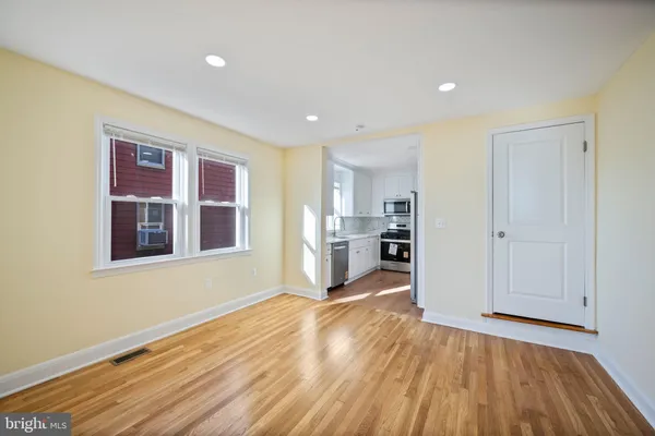 a view of empty room with wooden floor and kitchen