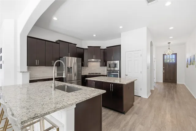 a kitchen with a stove a sink dishwasher a refrigerator and a dining table with wooden floor