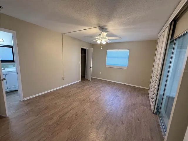 an empty room with wooden floor chandelier fan and windows