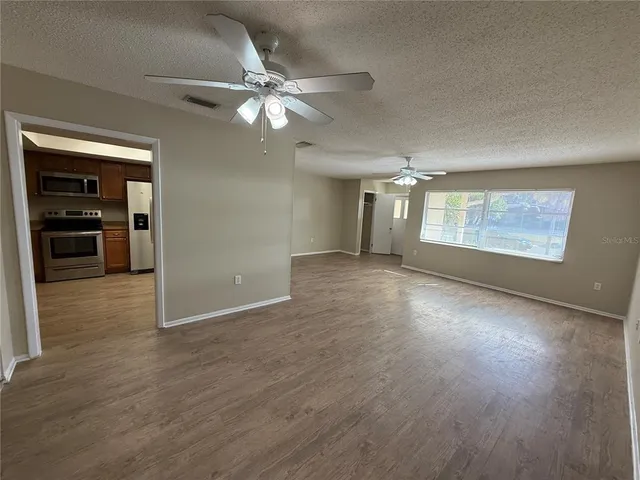 an empty room with wooden floor fan and windows