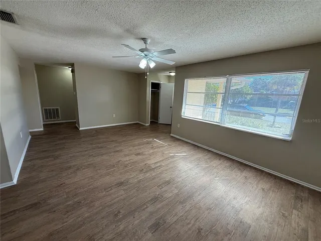 an empty room with wooden floor chandelier fan and windows
