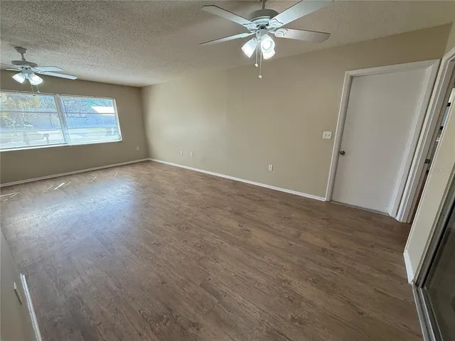 an empty room with wooden floor fan and windows