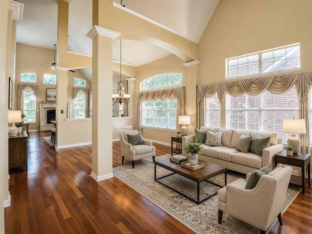 5708 Rickshaw Lane Plano, TX 75094 - Photo 4 of 28 Spacious living area featuring high vaulted ceilings, expansive windows, wood-finish flooring, architectural columns, and a fireplace with a mantel
